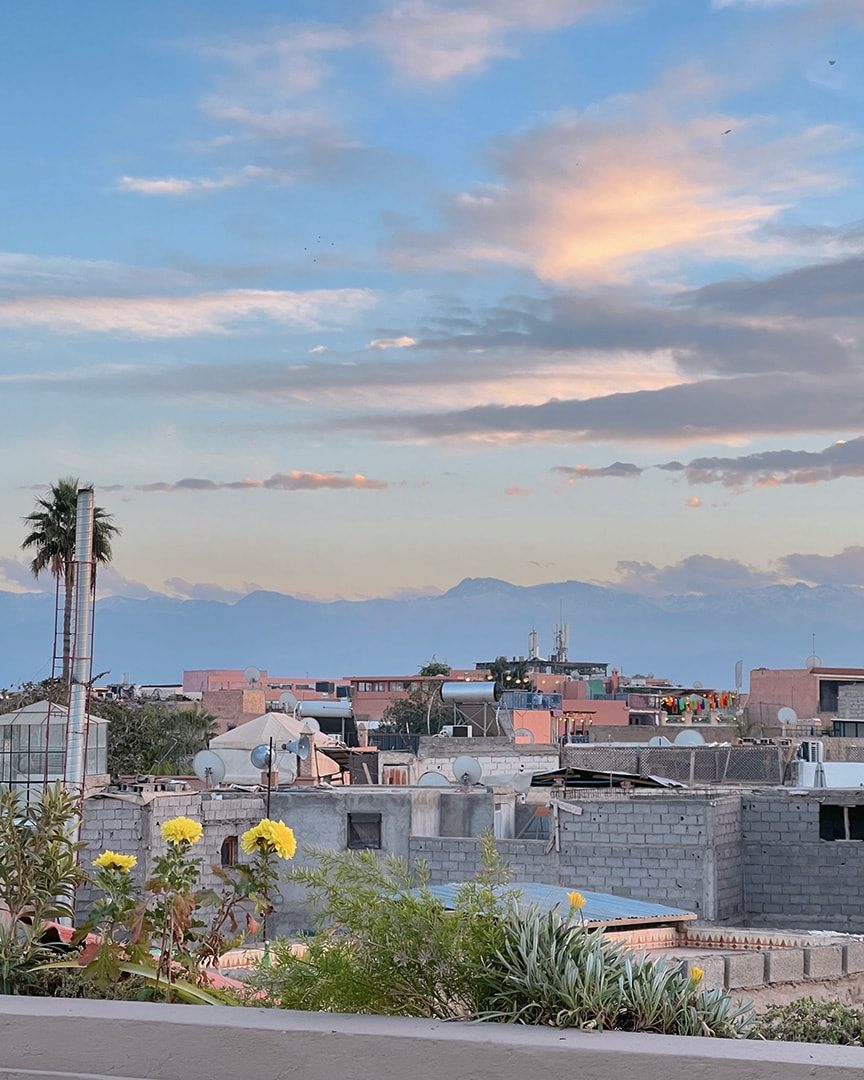 A scenic view over a Marrakech at twilight, with a mountain range in the background and a clear sky.