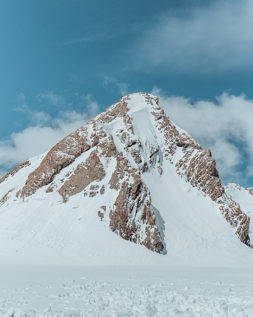 A solitary snow-covered peak pierces the sky, its steep slopes rising sharply against a backdrop of clear blue.