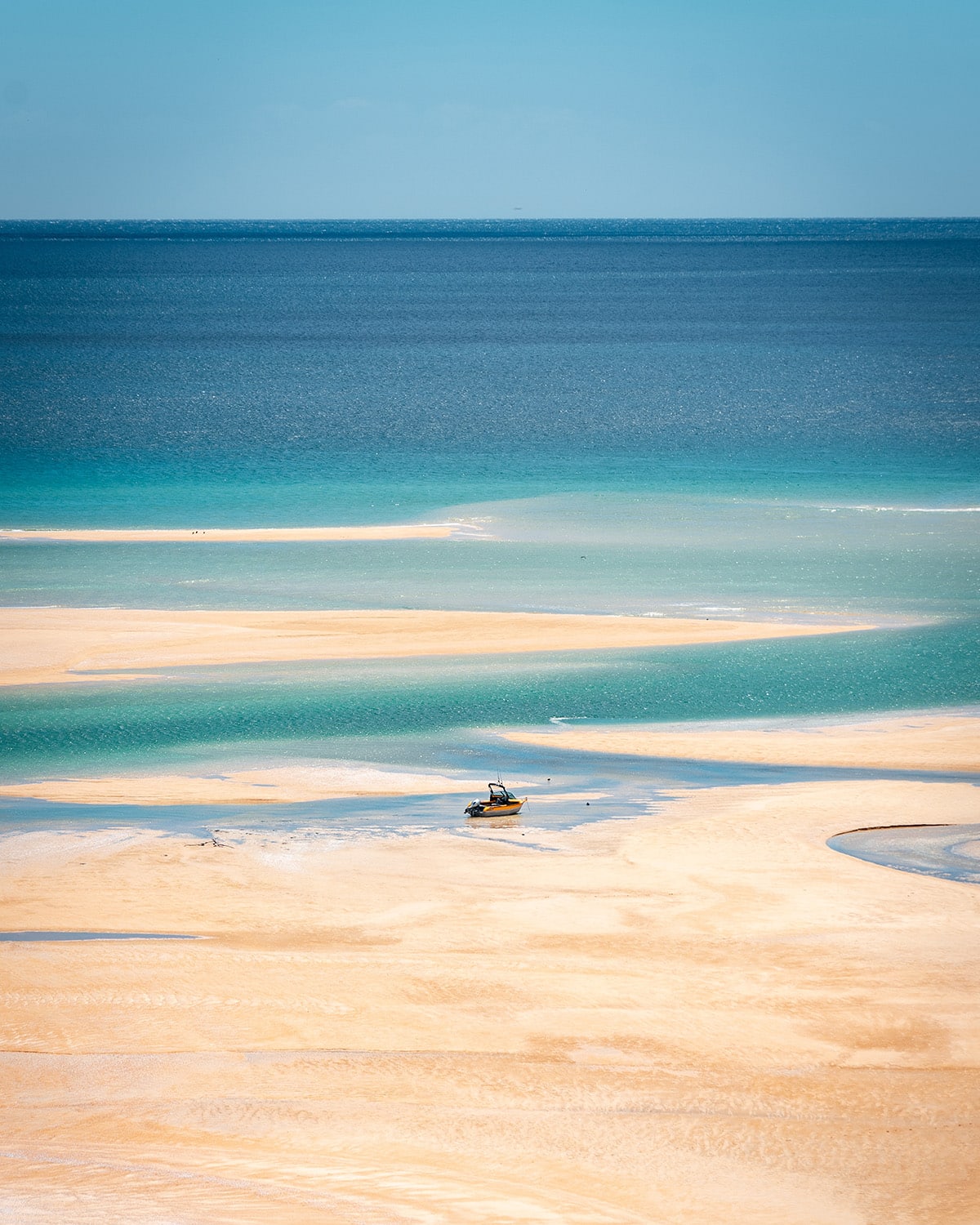 A shallow, multicolored coastal waterway with a small boat. Abel Tasman.