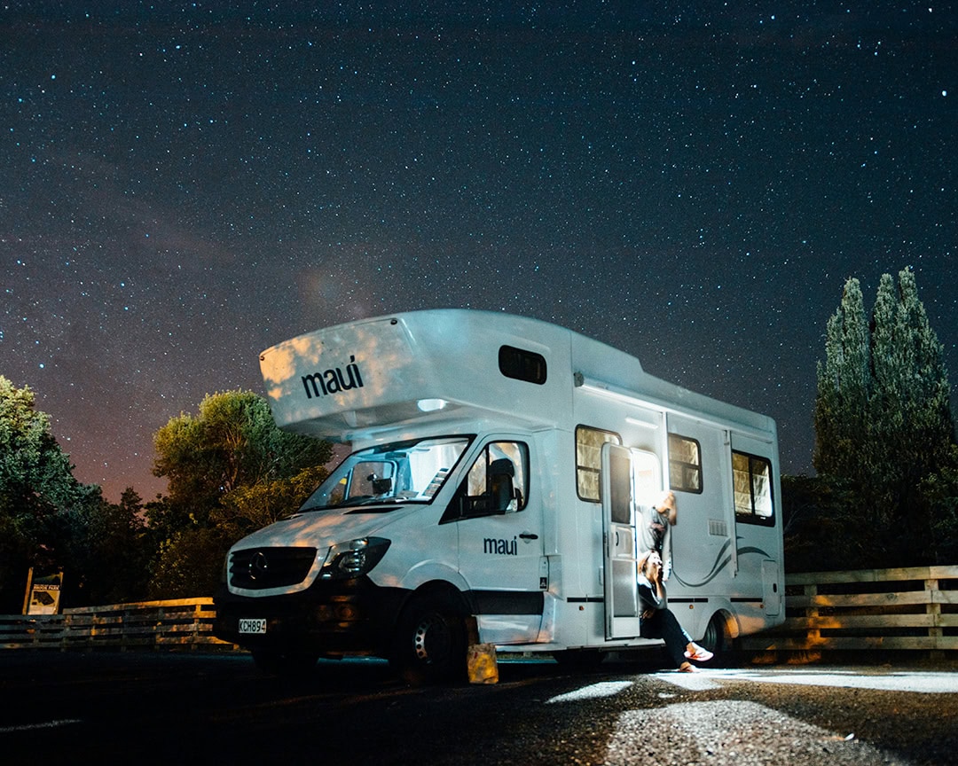 Under a starry night sky, a camper van is parked with its door open. Camping South Island.
