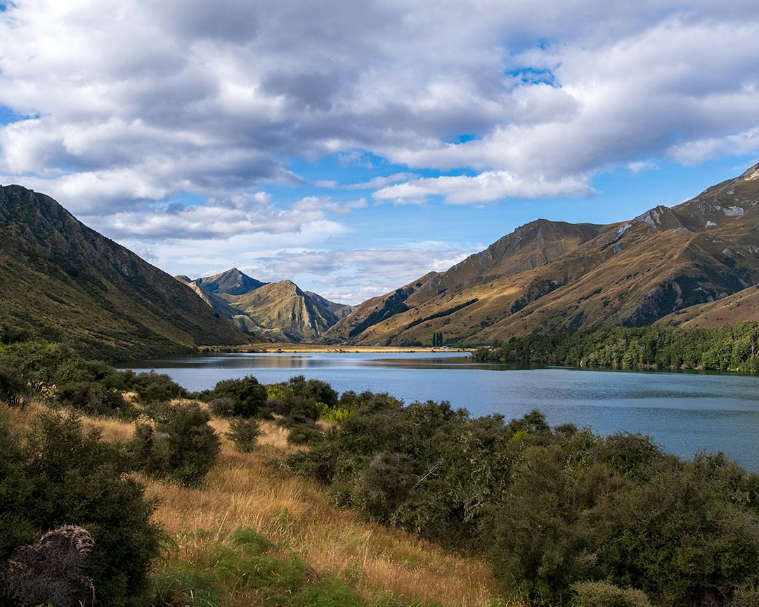 A sunny view of Moke Lake set amidst rolling hills and a blue sky. DOC campsite.