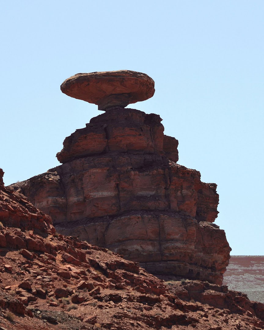A rock formation resembling an upside-down sombrero, balanced on a layered sandstone base.