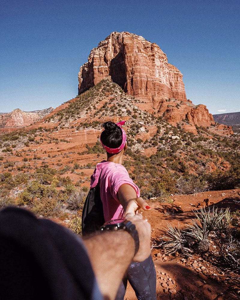 A woman holds hands with someone as she hikes toward a towering red rock formation in Sedona.