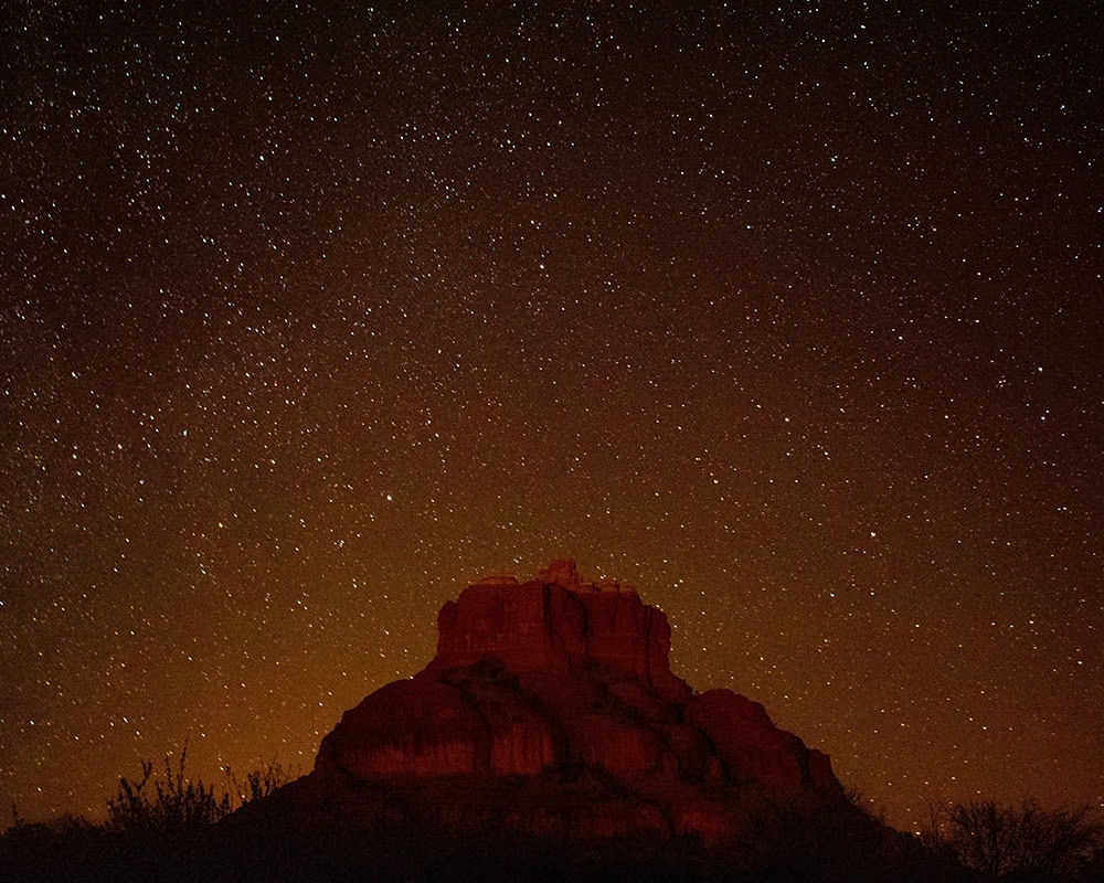 A red rock formation at night, with a night sky filled with thousands of bright stars.