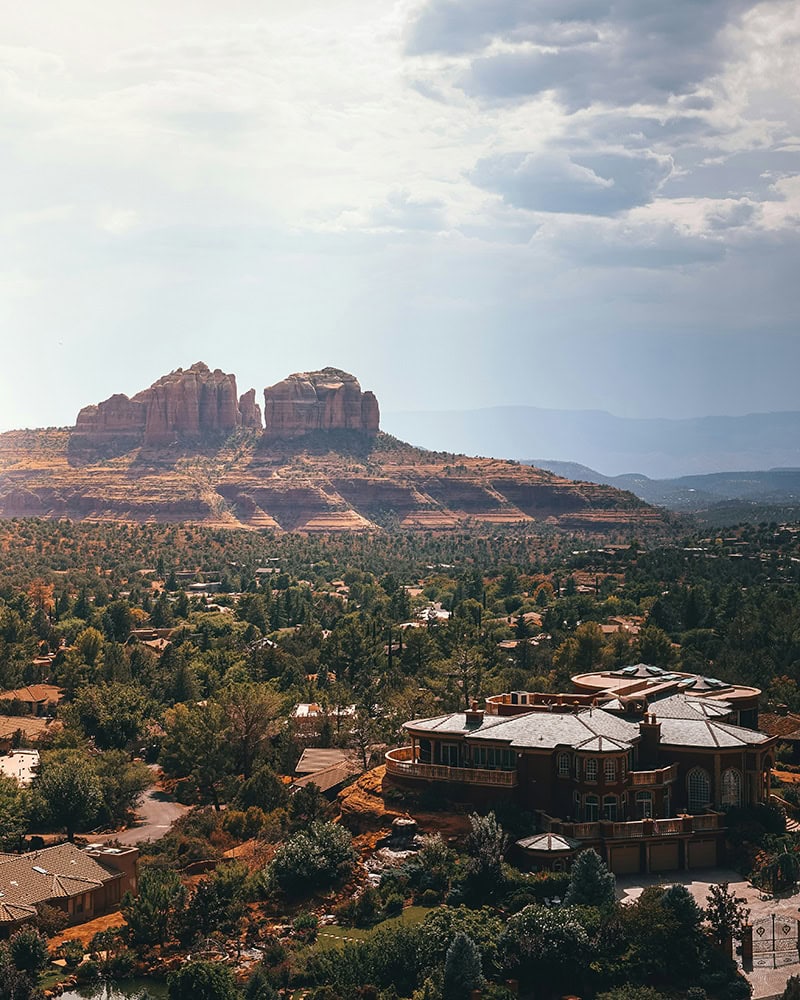 A scenic view of Sedona’s landscape, showing red rock formations and a valley filled with houses and trees.
